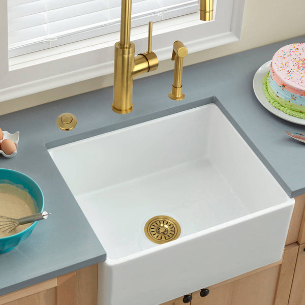 White kitchen sink with gold faucet and drain in a modern kitchen setting.