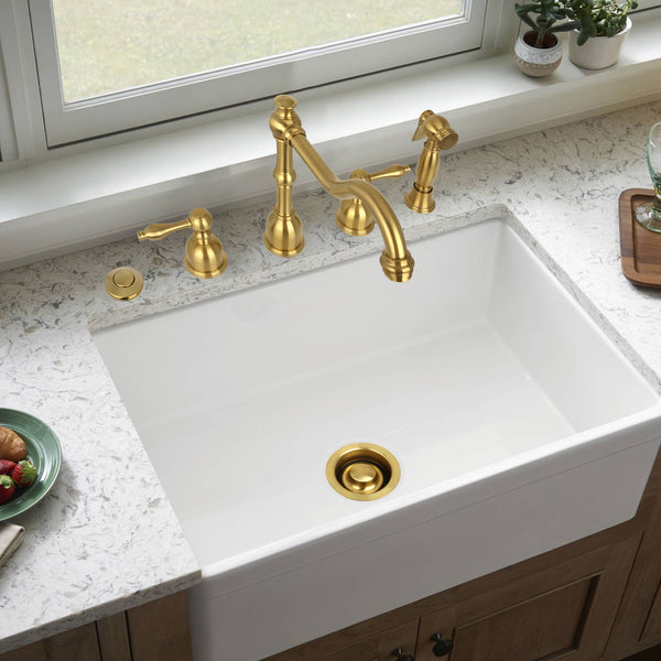 White kitchen sink with gold faucet and handles in a bright kitchen setting.