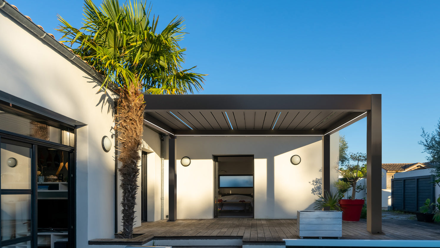 Modern house exterior with a covered patio and palm tree under a clear blue sky.